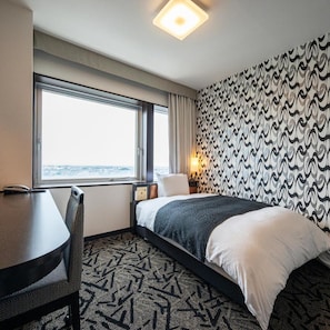 Une chambre d’hôtel avec un lit, un bureau, une chaise, une fenêtre donnant sur un paysage agréable et un papier peint à motifs.