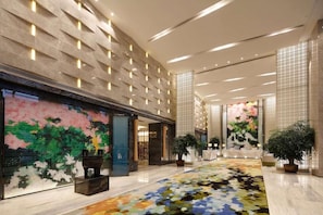 Un hall espacioso con piso estampado, un mural grande en la pared y plantas en macetas.
