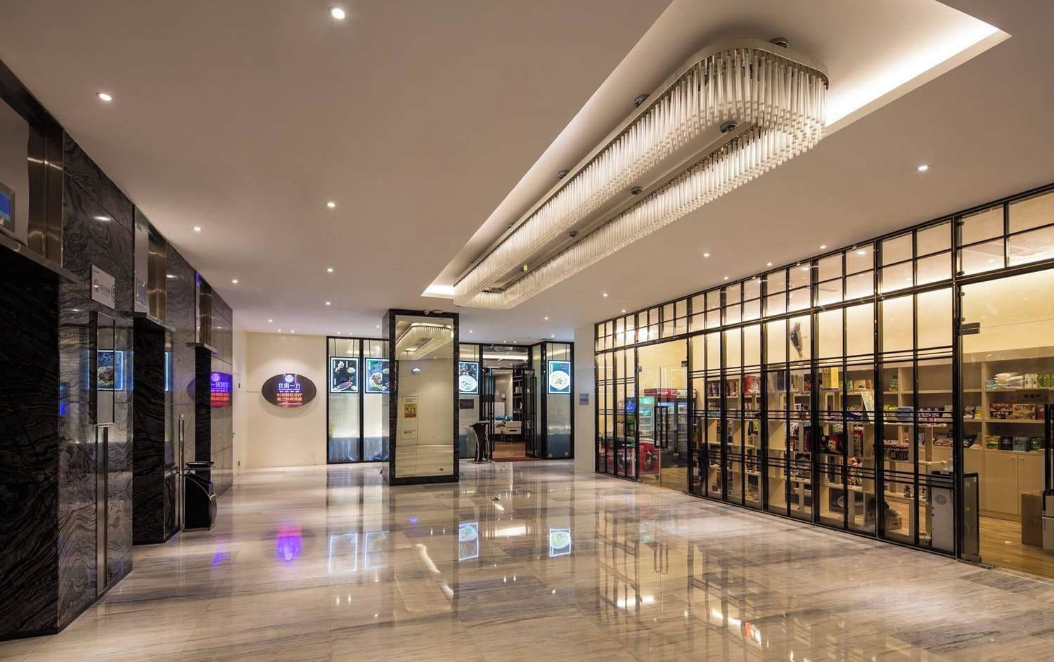 A modern hotel lobby with a polished marble floor, a large chandelier, and glass storefronts.