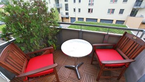 A balcony with a round table and two wooden chairs with red cushions. - Richie Apartment Near Aquapark (Prague)