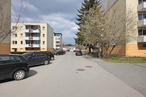 Une rue résidentielle bordée d’arbres, avec des voitures garées, des immeubles d’habitation et un trottoir.