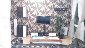 A living room with a flat-screen TV, a coffee table, a potted plant, and a leather sofa. - Richie Apartment Near Aquapark (Prague)