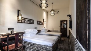 Een hotelkamer met een bakstenen muur, twee bedden, een houten bureau en hangende吊り下げ式ラ  ンプ.