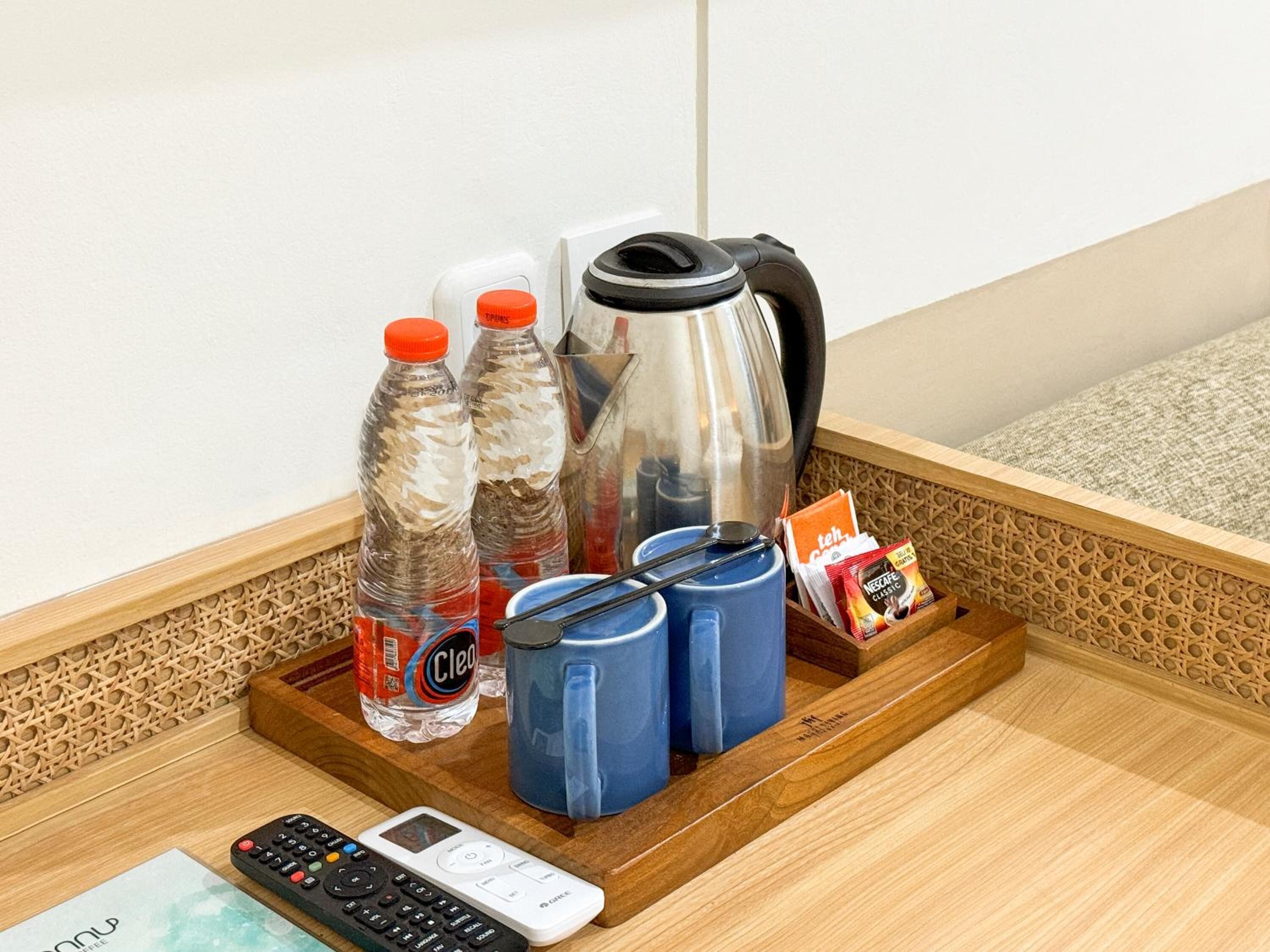 A hotel room's minibar with bottled water, coffee mugs, a kettle, a remote control, and a card holder.