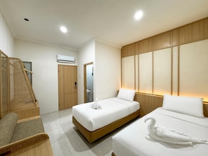 Habitación de hotel con dos camas, un armario de madera, una pequeña zona de estar y un baño visible a través de una puerta abierta.