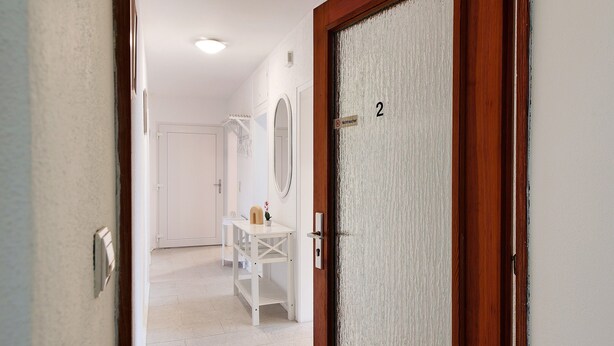 Un couloir avec une porte blanche portant le numéro « 2 » et une table blanche sur laquelle se trouvent un miroir et une petite plante.