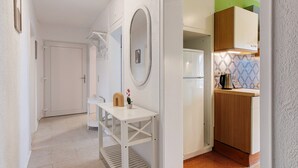 Un couloir mène à une cuisine : on y trouve une porte blanche, une petite table avec un vase et un miroir accroché au mur.