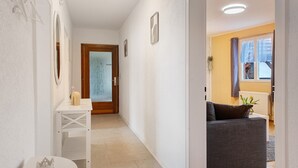 Un couloir avec une porte blanche, une table blanche ornée d’un objet décoratif et un canapé gris dans la pièce adjacente.