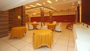 A banquet hall with round tables covered in yellow tablecloths and white chairs, a red brick wall, and a chandelier. - OYO 11451 Hotel Auston (Gurugram)