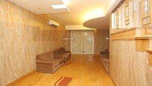 A spacious living area with a wooden floor, a sofa set, and a large sliding glass door leading to a balcony. - OYO 11451 Hotel Auston (Gurugram)