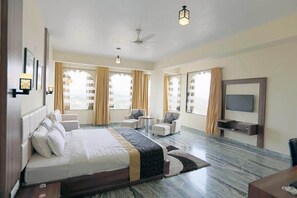 Una habitación de hotel espaciosa con una cama grande, televisión, ventilador de techo y una zona de estar con sillones.