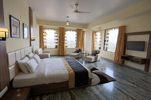 A hotel room with a large bed, two armchairs, a small table, a TV, and a view of the outdoors. - Regenta Central Mewargarh (Udaipur)
