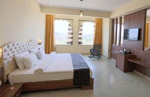 A hotel room with a large bed, a TV mounted on the wall, a small seating area, and a window with curtains. - Regenta Central Mewargarh (Udaipur)