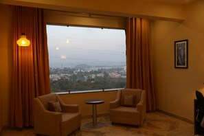 Una habitación con dos sofás, una mesita redonda, una ventana con cortinas y un cuadro en la pared.