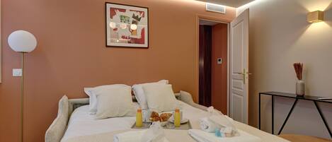 A hotel room with a bed, bedside table, and a framed picture on the wall.