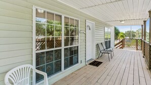 Une véranda couverte avec une terrasse en bois, de grandes fenêtres et une porte.