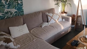 Un salon avec un canapé beige, une plante en pot, une lampe et des tableaux encadrés accrochés au mur.