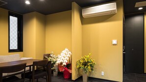 A room with a dining table, chairs, a sofa, and two flower arrangements. - Doyanen Hotels Kingyo (Osaka)