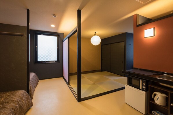 Habitació d'hotel compacta amb una porta corredissa que dona a un balcó, una cuineta amb microones i bullidor, i una finestra gran amb un dibuix de quadres.