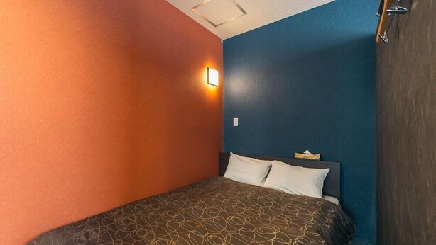 A hotel room with a bed, a nightstand, and a wall-mounted light. - Doyanen Hotels Kingyo (Osaka)