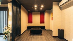 A modern hotel lobby with a dark wood bench, a red accent wall, and a large air conditioning unit. - Doyanen Hotels Kingyo (Osaka)