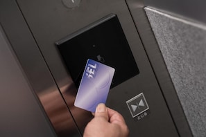 Une main tenant une carte de crédit insérée dans le lecteur de cartes d’un ascenseur.