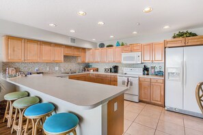 Eine moderne Küche mit Holzausstattung, einer großen Kochinsel mit Barhocker, einem weißen Kühlschrank und einer Mikrowelle.