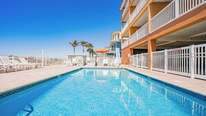 A clear blue pool with white lounge chairs and umbrellas, surrounded by a white fence and palm trees. - Casa de Playa 206 - Beach Front Condo (Indian Rocks Beach)