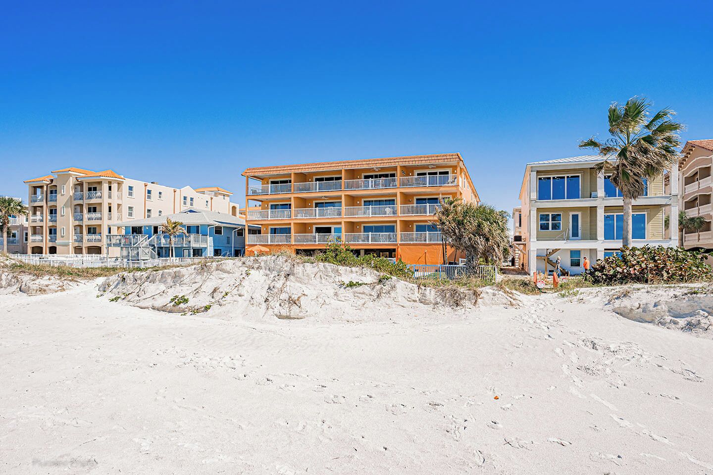 Een hotel aan het strand met meerdere verdiepingen, balkons en een zandstrand op de voorgrond.