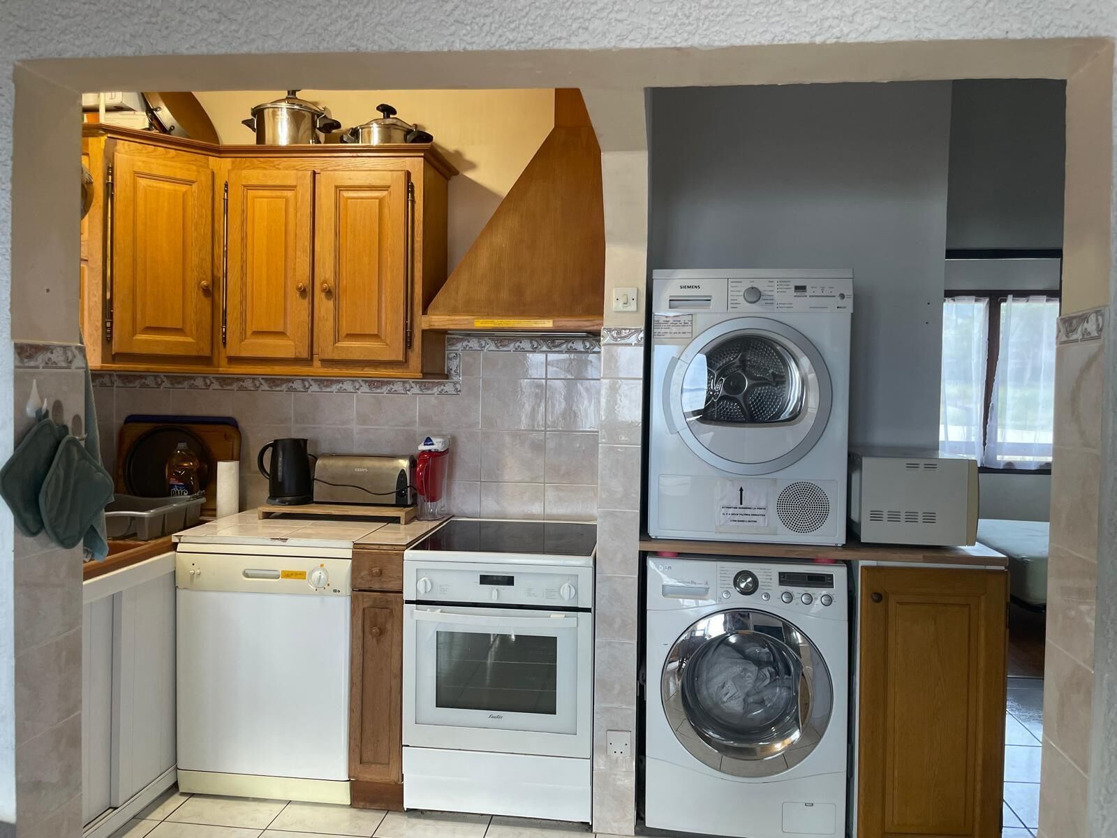 A compact kitchen with wooden cabinets, a dishwasher, a built-in oven, and a front-loading washing machine.