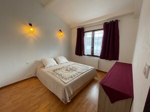 Una camera da letto con un letto, due luci a parete, una finestra con tende e un termosifone.
