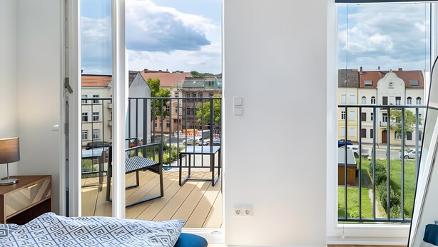 Ein Zimmer mit Bett, Nachttisch, Fenster mit Balkonblick und einer Tür zu einem Außenbereich.