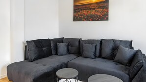 Ein modernes Wohnzimmer mit einem Ecksofa, einem runden Couchtisch und einem Gemälde, das einen Sonnenuntergang über einem Blumenfeld zeigt.