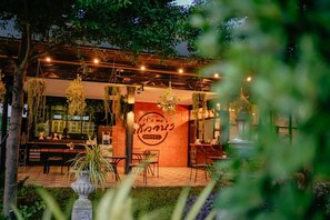 An outdoor seating area with hanging plants, a brick wall with a hotel sign, and a well-lit patio. - IT Me Keawanong Hotel (Nakhon Ratchasima)