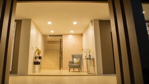 A modern hotel lobby with a staircase, a checkered armchair, and a small table with a vase of flowers. - IT Me Keawanong Hotel (Nakhon Ratchasima)