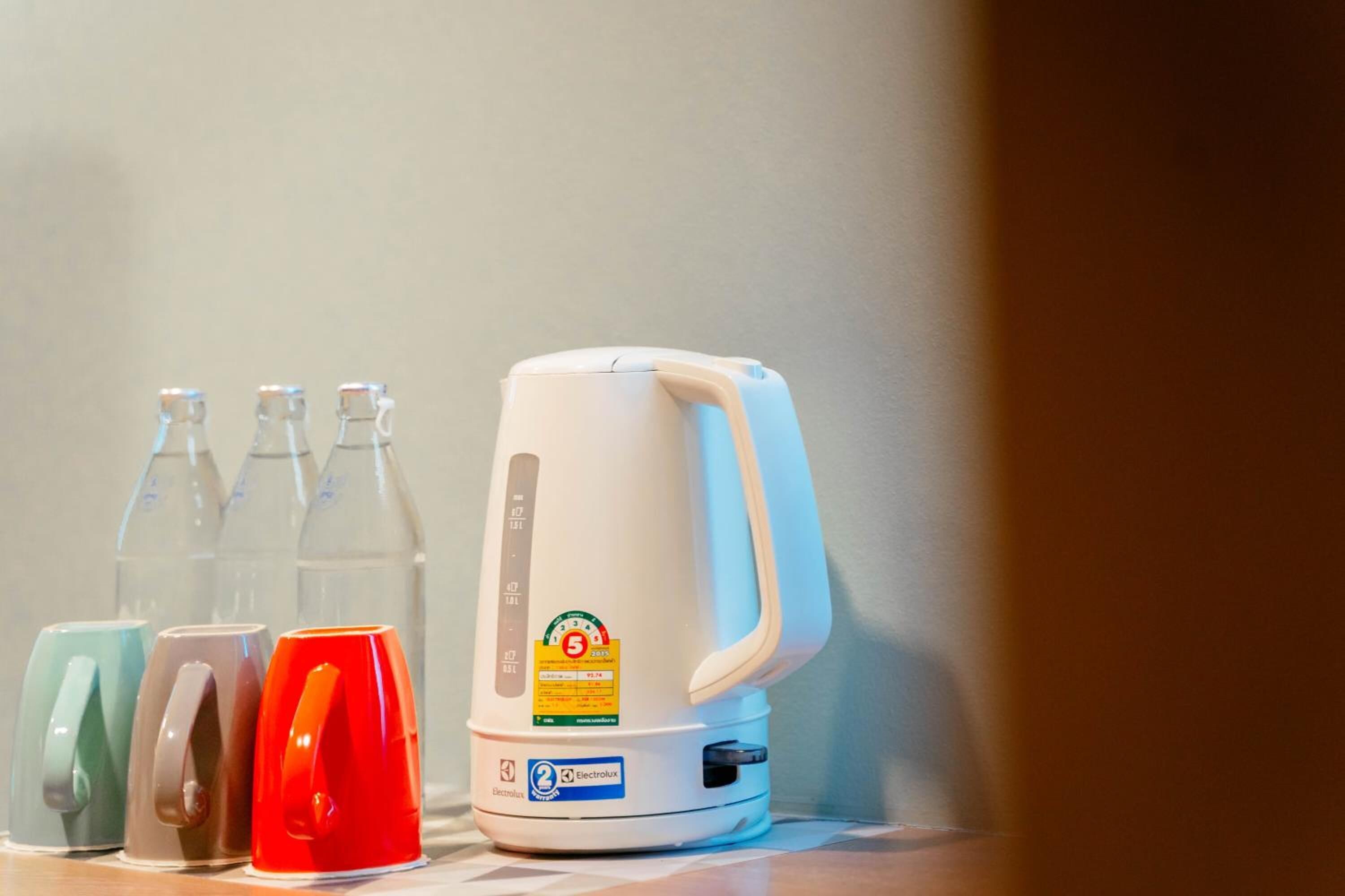 Una tetera blanca con pantalla digital y panel de control, junto con tres tazas de colores.