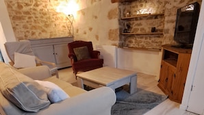 A cozy living room with a stone wall, a sofa, a red chair, a wooden coffee table, and a television. - Sunset de Bénévent, country cottage for 4 to 6 people (Bénévent-l'Abbaye)