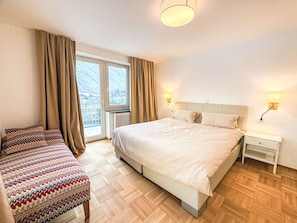 Habitación de hotel con una cama grande, dos mesitas de noche, una ventana con cortinas y vistas a las montañas.
