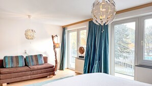 A bedroom with a large bed, a brown sofa with patterned cushions, a hanging light fixture, and a view of trees through the window. - Acereto by Interhome (Nassereith)