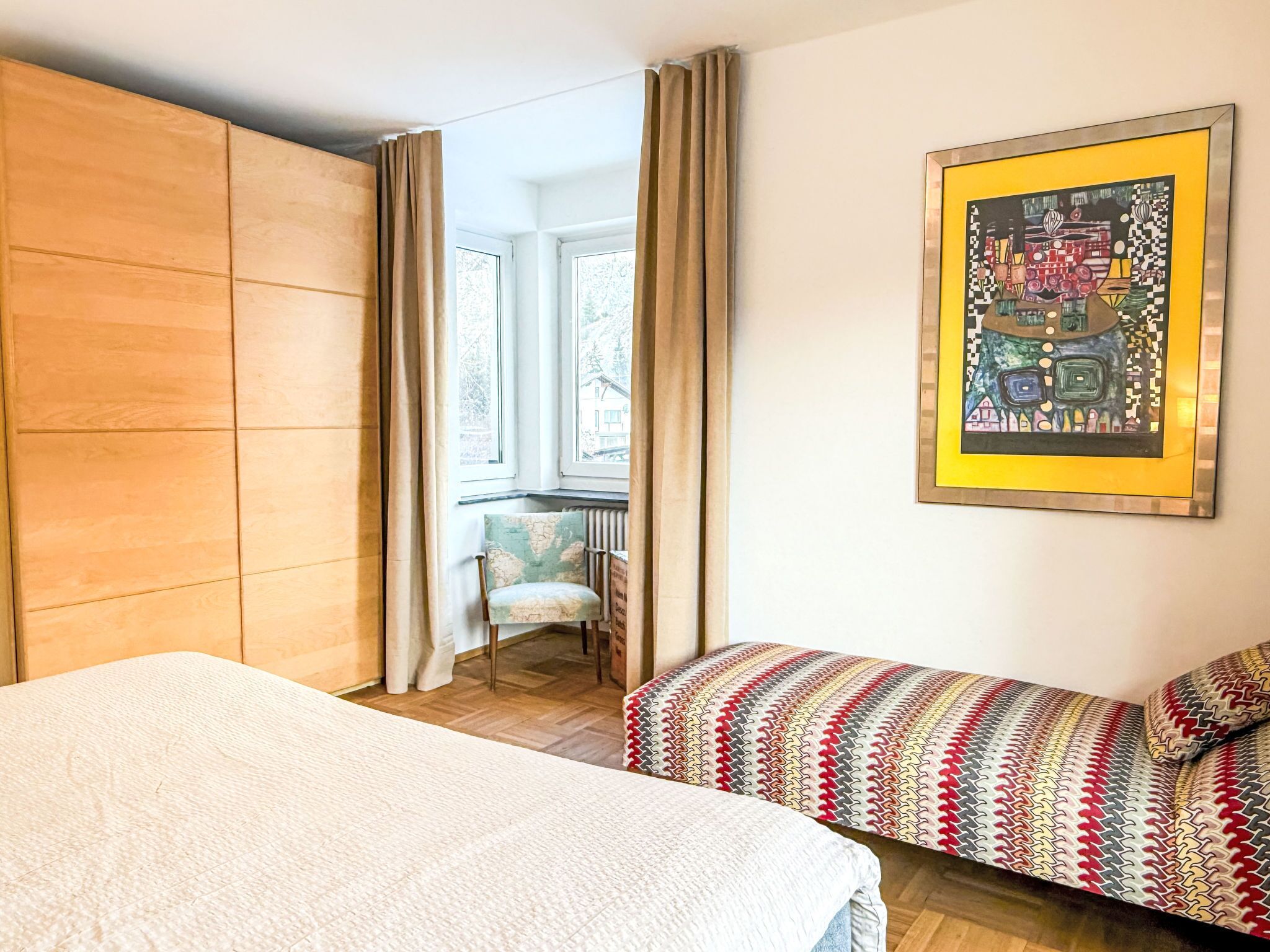 Ein Zimmer mit einem Bett, einem Sofa, einem Sessel, einem Heizkörper und einem Fenster mit Vorhängen.