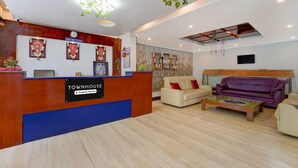 A reception area with a wooden reception desk labeled "Townhouse Company Serviced." There are framed pictures on the wall, a clock, and a sofa with red cushions. - Classic Abirami Grand Inn (Kodaikanal)