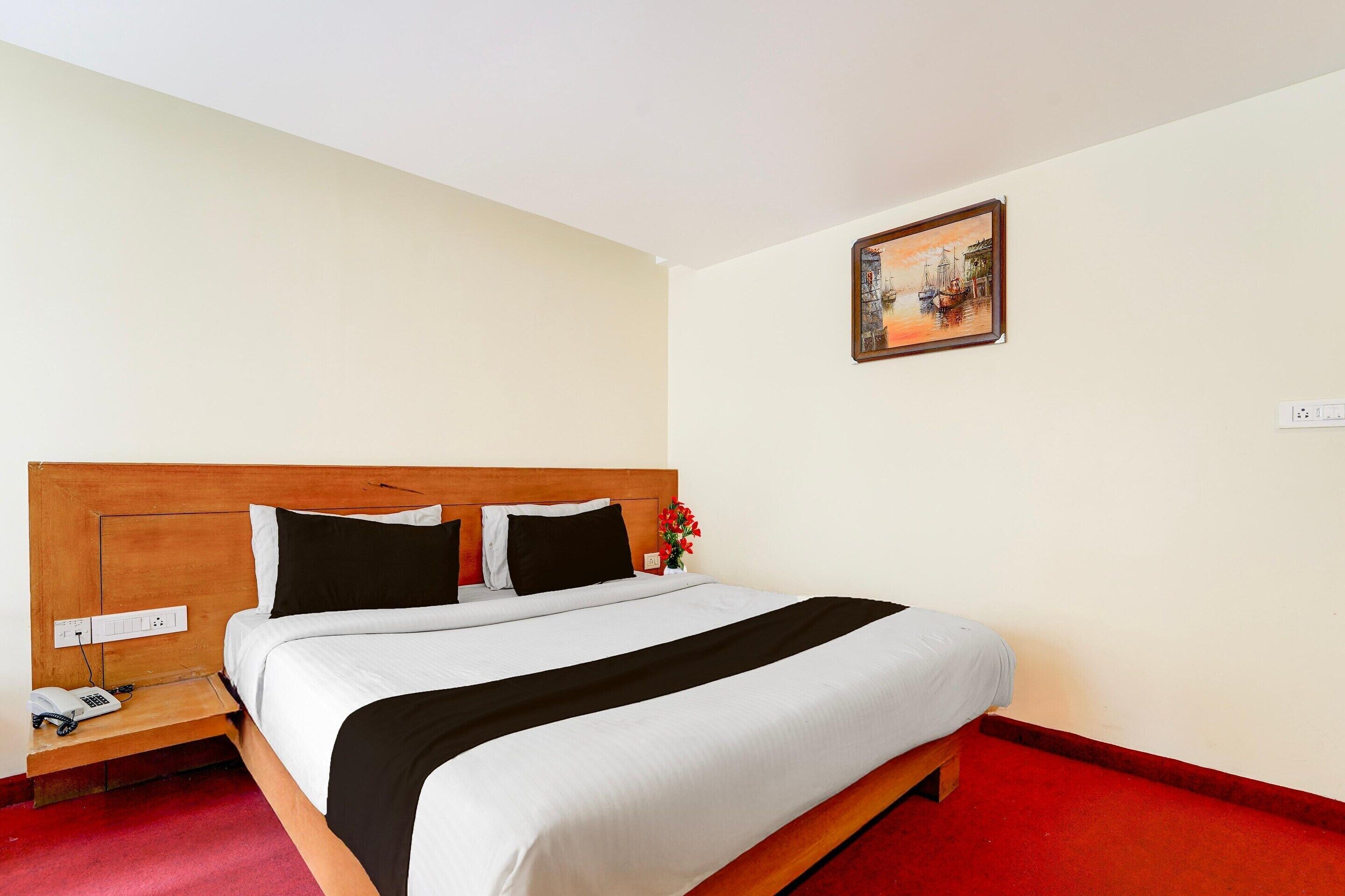 A neatly made bed with a wooden headboard, a bedside table with a phone, and a painting on the wall.