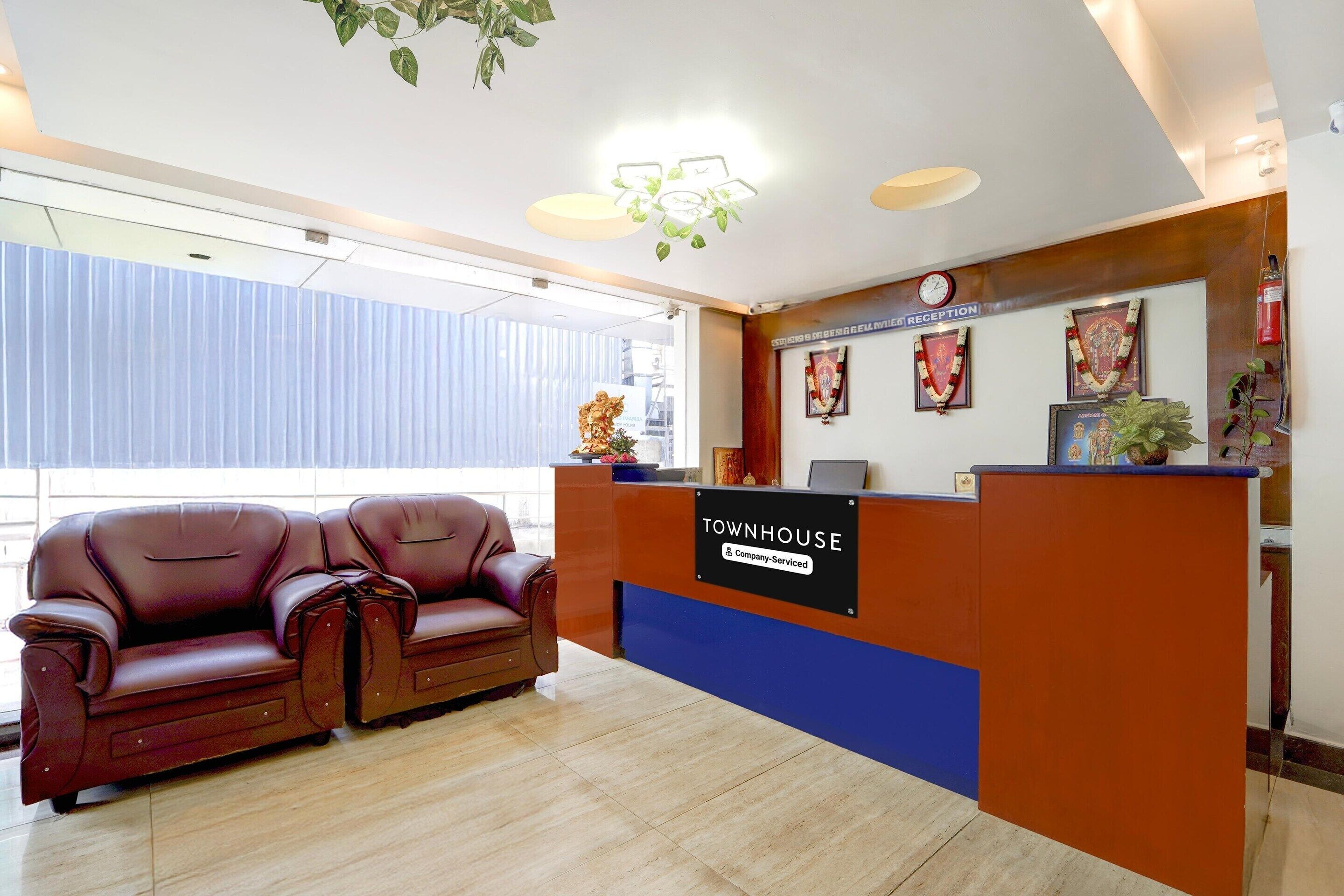 Una zona de recepción con un sofá de cuero marrón, un mostrador de recepción que dice "TOWNHOUSE & Company Serviced" y un reloj en la pared.