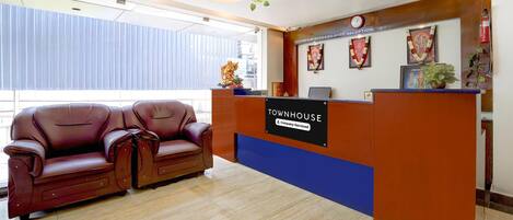 Una zona de recepción con un sofá de cuero marrón, un mostrador de recepción que dice "TOWNHOUSE & Company Serviced" y un reloj en la pared.
