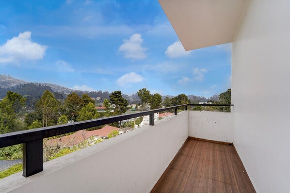 Un balcon doté d’un plancher en bois et d’une rambarde noire, offrant une vue sur un quartier résidentiel avec des arbres et des maisons, le tout sous un ciel bleu dégagé.