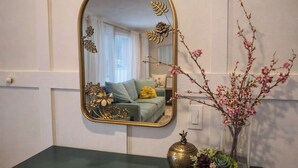 Une salle de bain avec un plan de toilette vert, un miroir encadré d’or et un vase contenant des fleurs roses.