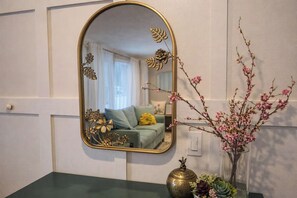 Ein Badezimmer mit einer grünen Ablagefläche, einem goldfarben gerahmten Spiegel und einer Vase mit rosa Blumen.