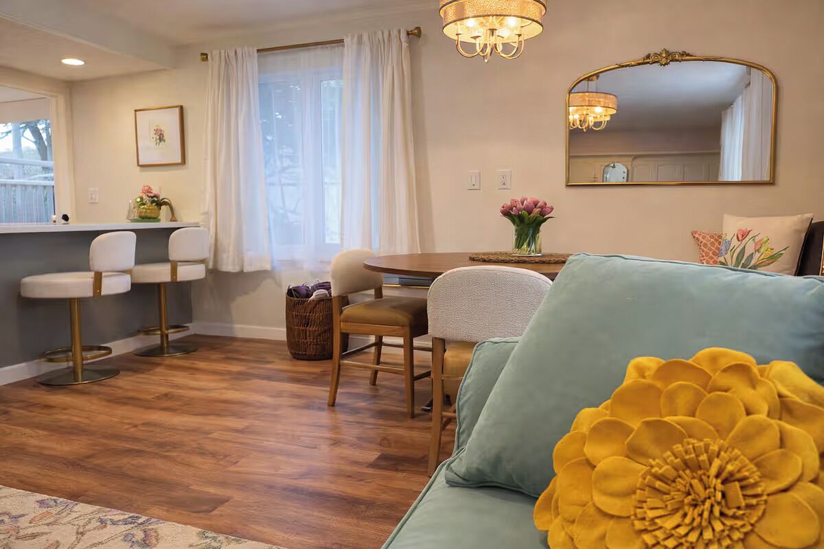 Ein gemütliches Wohnzimmer mit einer Couch, einem Esstisch mit Stühlen, einer Deckenleuchte und einem großen Spiegel an der Wand.