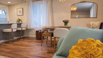 Ein gemütliches Wohnzimmer mit einer Couch, einem Esstisch mit Stühlen, einer Deckenleuchte und einem großen Spiegel an der Wand.