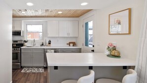 Une cuisine moderne avec des armoires blanches, un plafond en bois et un grand îlot central doté de tabourets de bar.